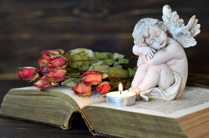 Enon UMC Bereavement Committee beautiful picture of resting angel sitting on top of open Bible; also on Bible is lighted tea candle and dried roses